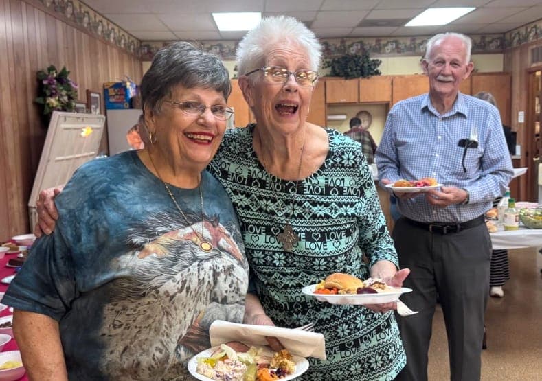 Two friends laughing together over dinner in the fellowship hall